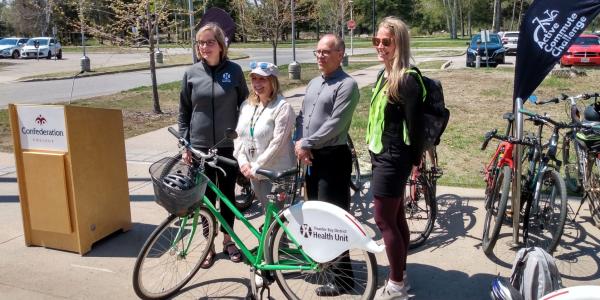 representatives from TBDHU, City of Thunder Bay and Confederation College pose in front of a bicycle
